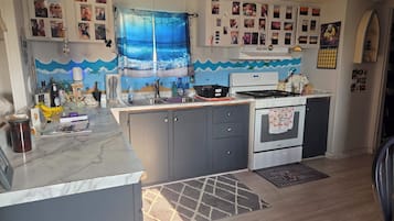 Cuina compacta amb forn integrat, un rentapeus i un taulell. Hi ha armaris a la part superior del taulell, i una cortina decorativa amb un dibuix de ones.