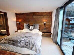 A bedroom with a large bed, wooden headboard, two wall-mounted lights, and a view of a cabin through a glass door. - Heinrida Appartement/Fewo 10-Bettwohnung by Interhome (Saas-Fee)