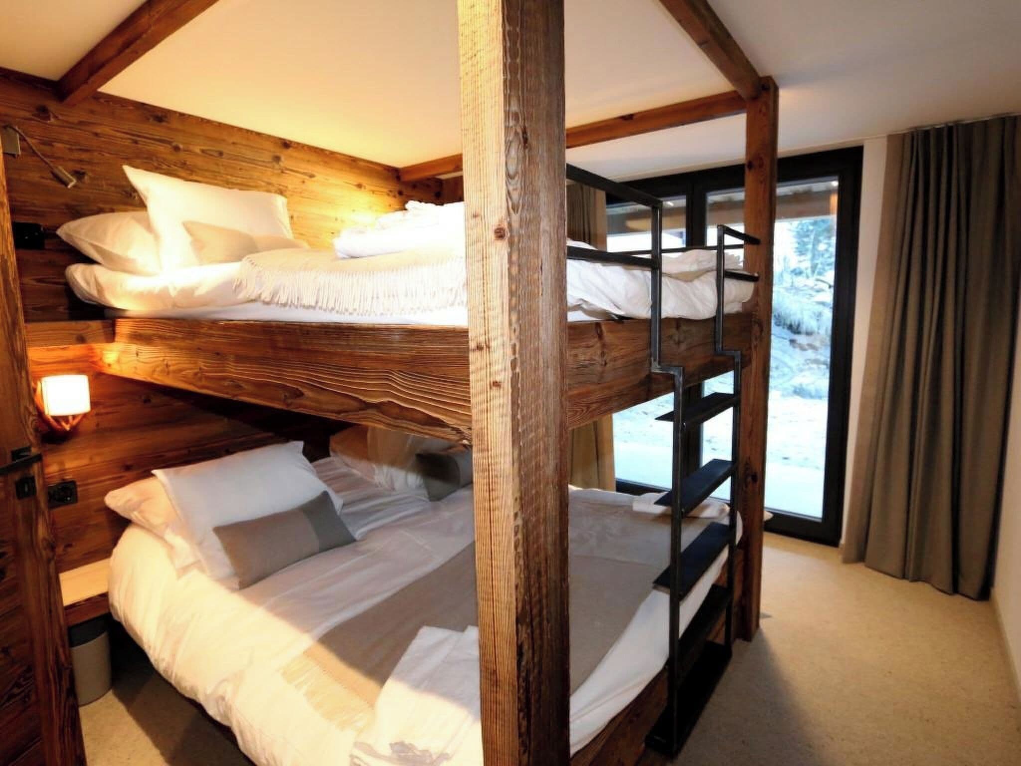 Habitación con literas, vigas de madera, una ventana con cortinas y una lámpara a la izquierda.