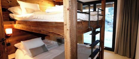 Habitación con literas, vigas de madera, una ventana con cortinas y una lámpara a la izquierda.