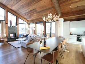 A spacious living area with a fireplace, a dining table, and a kitchen in the background. - Heinrida Appartement/Fewo 10-Bettwohnung by Interhome (Saas-Fee)