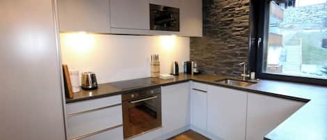A modern kitchen with white cabinets, a built-in oven, a sink, and a stone accent wall.