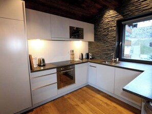 A modern kitchen with white cabinets, a built-in oven, a sink, and a stone accent wall. - Heinrida Appartement/Fewo 10-Bettwohnung by Interhome (Saas-Fee)