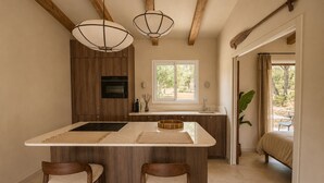 A kitchen with wooden cabinets, a central island with stools, pendant lighting, and a view to an outdoor seating area. - Casa di Luce - Hot tub & beach within walking distance, ocean view (Corbara)