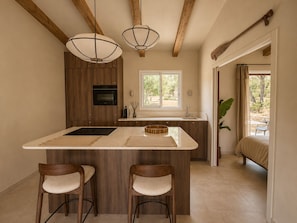 A kitchen with wooden cabinets, a central island with stools, pendant lighting, and a view to an outdoor seating area. - Casa di Luce - Hot tub & beach within walking distance, ocean view (Corbara)