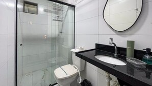 Moderni kylpyhuone, jossa on lasinen suihkuseinä, valkoinen wc-istuin, musta pesuallas, jonka yläpuolella on peili, sekä wc-paperiteline.