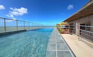 Una piscina azul cristalina con borde de azulejos, barandilla metálica y vista al océano.