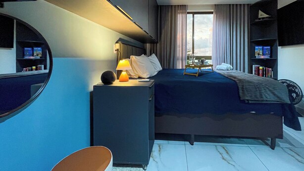 Habitación de hotel moderna con cama, mesita de noche, lámpara y vistas al exterior.