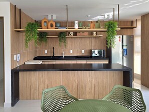 A modern kitchen with a central island, wooden cabinetry, and hanging plants. - Dva Flats By Hosppedar (Cabedelo)