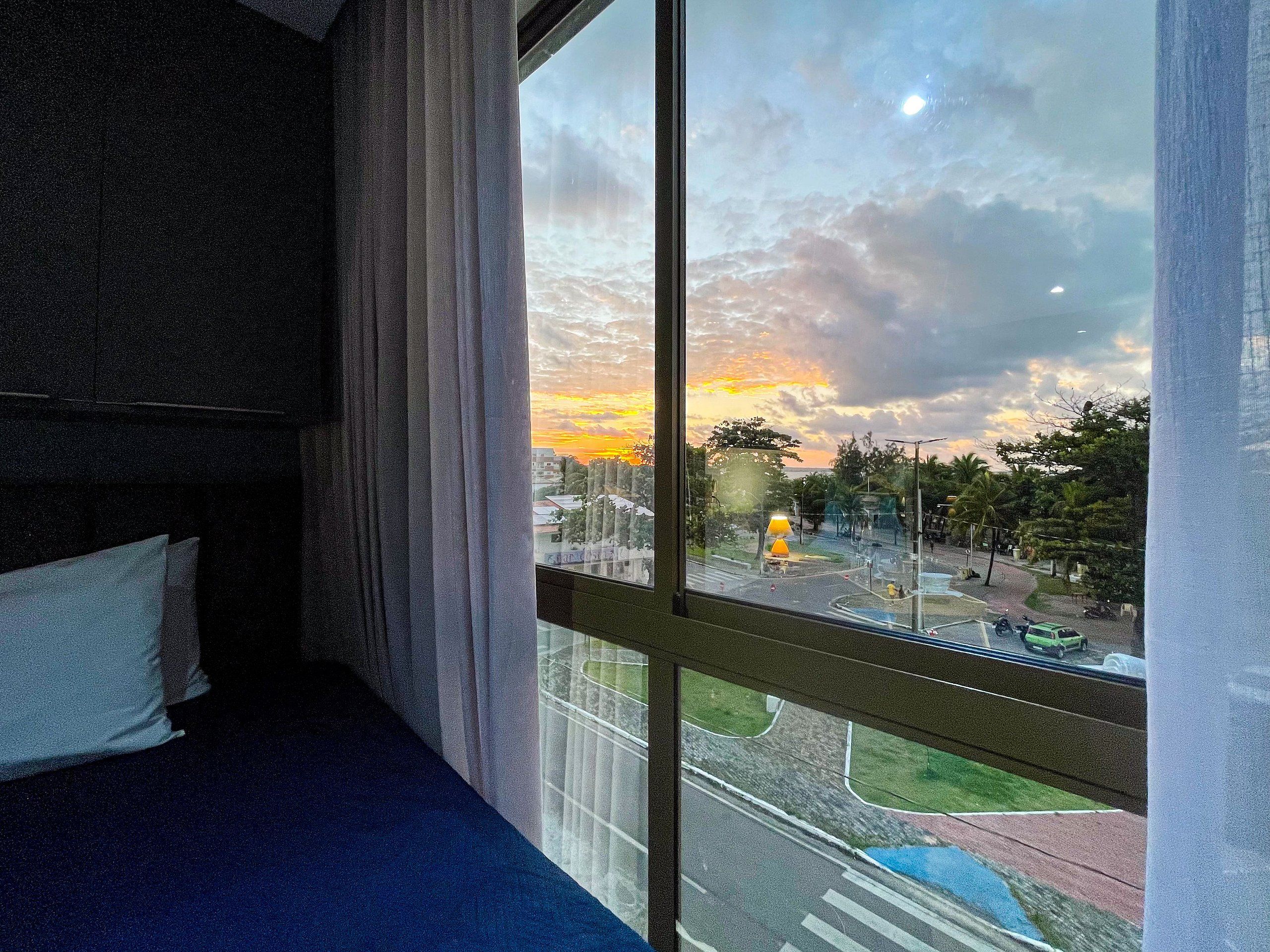 A room with a large window overlooking a street and a sunset.