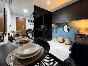 Un comedor moderno con una mesa redonda para dos personas, una cocina al fondo y una cama con una mesita de noche.