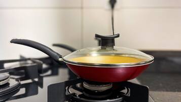Een rode pan op een gasfornuis met een glazen deksel, een stopcontact en een zwart kookoppervlak.