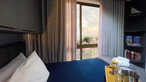 Habitación de hotel con cama, televisor, estantería y ventana con cortinas.