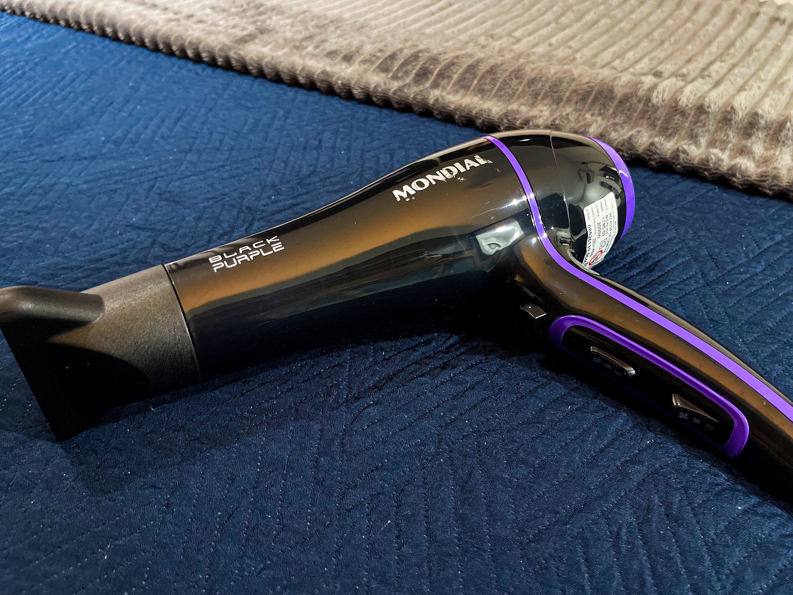 Un secador de pelo negro y morado con el nombre de marca 'MONDIAL' sobre una superficie azul con textura.
