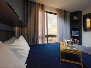 Habitación de hotel con cama, una mesita de madera con una bandeja, una estantería y vistas al exterior.