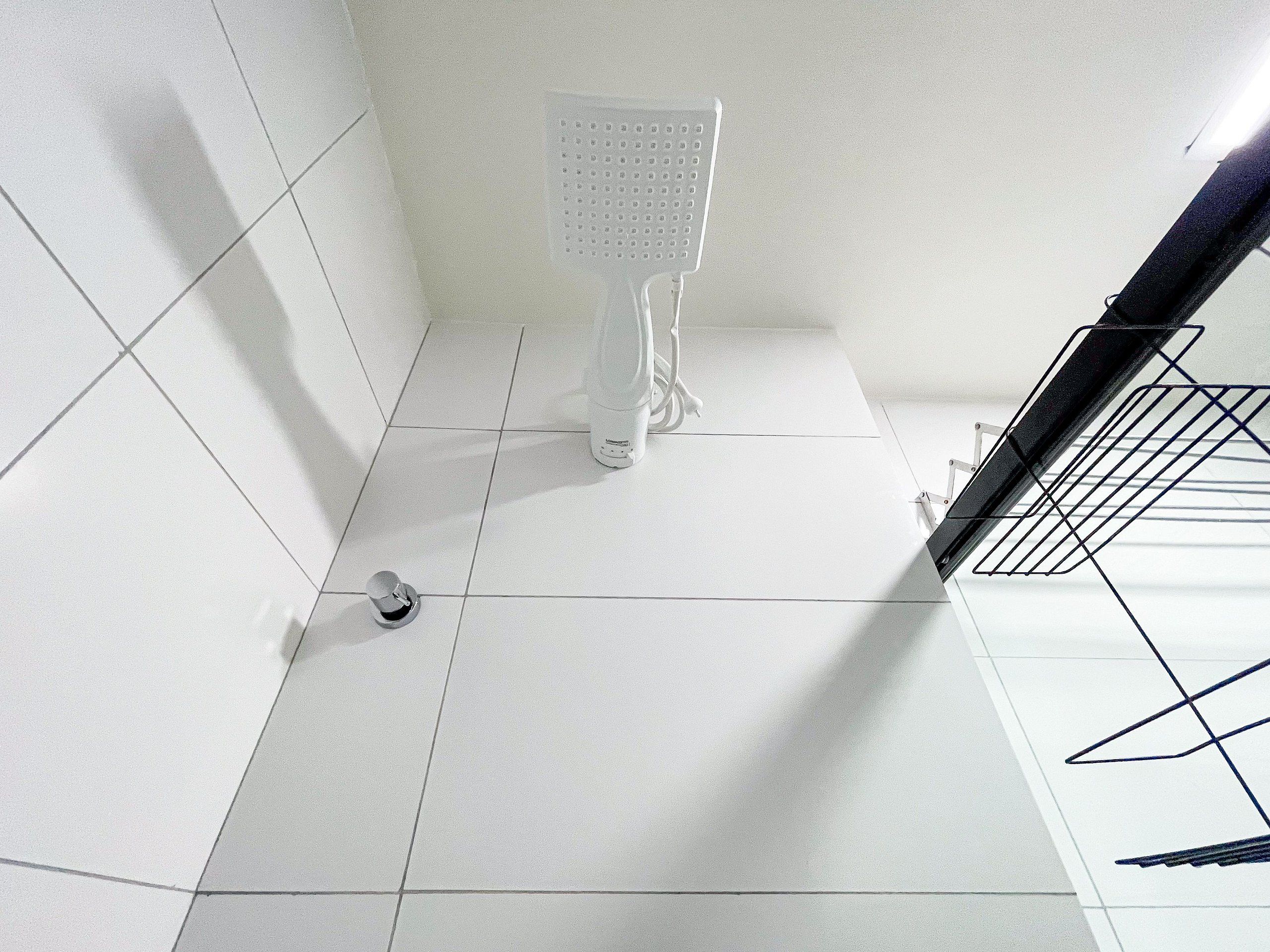 Un baño con piso de baldosas blancas, inodoro y zona de ducha.