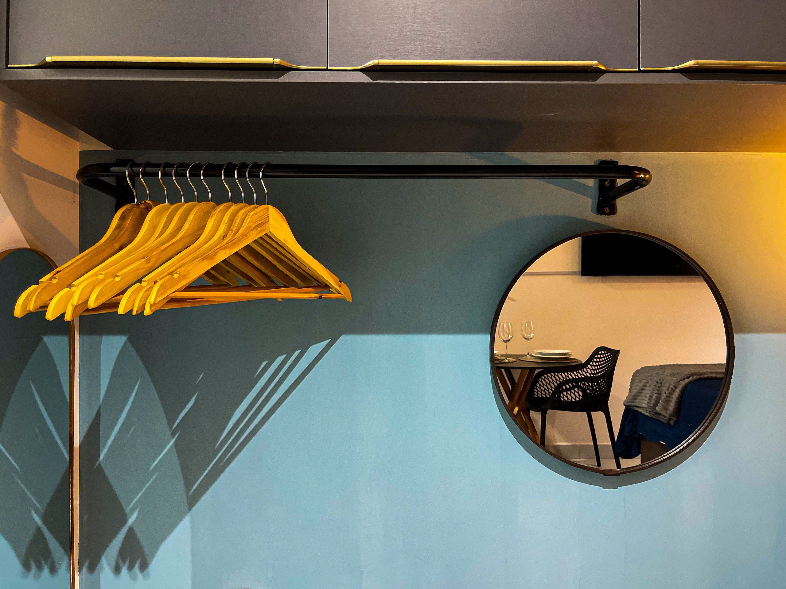 A room with a mirror, a coat rack with hangers, and a chair.