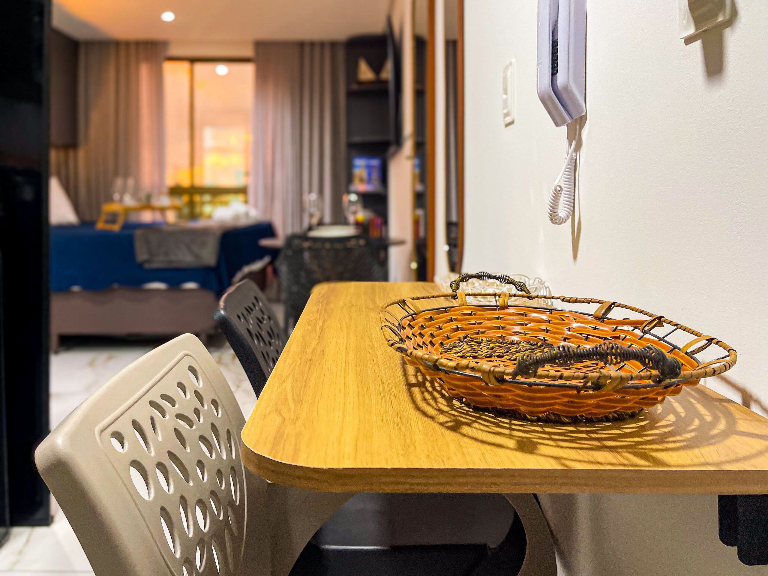 Una habitación de hotel con una mesa de madera, una cesta tejida y una silla blanca.