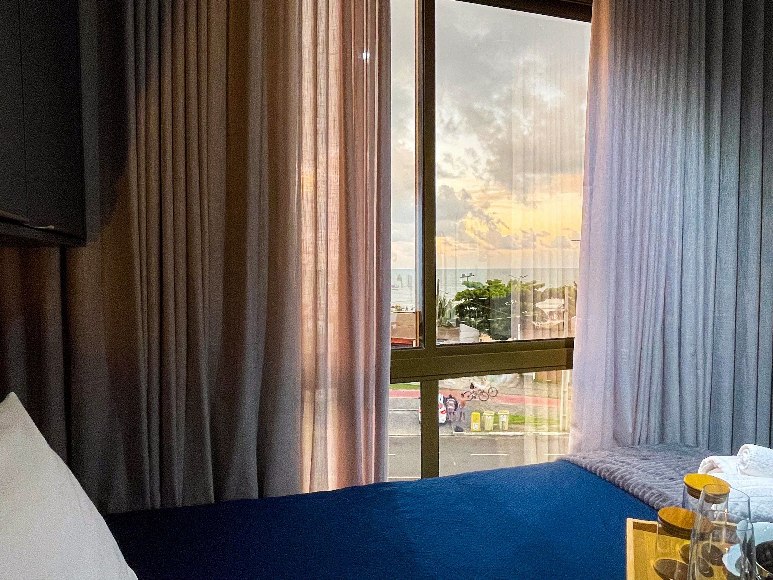 A hotel room with a bed, a window with curtains, and a view of the street outside.