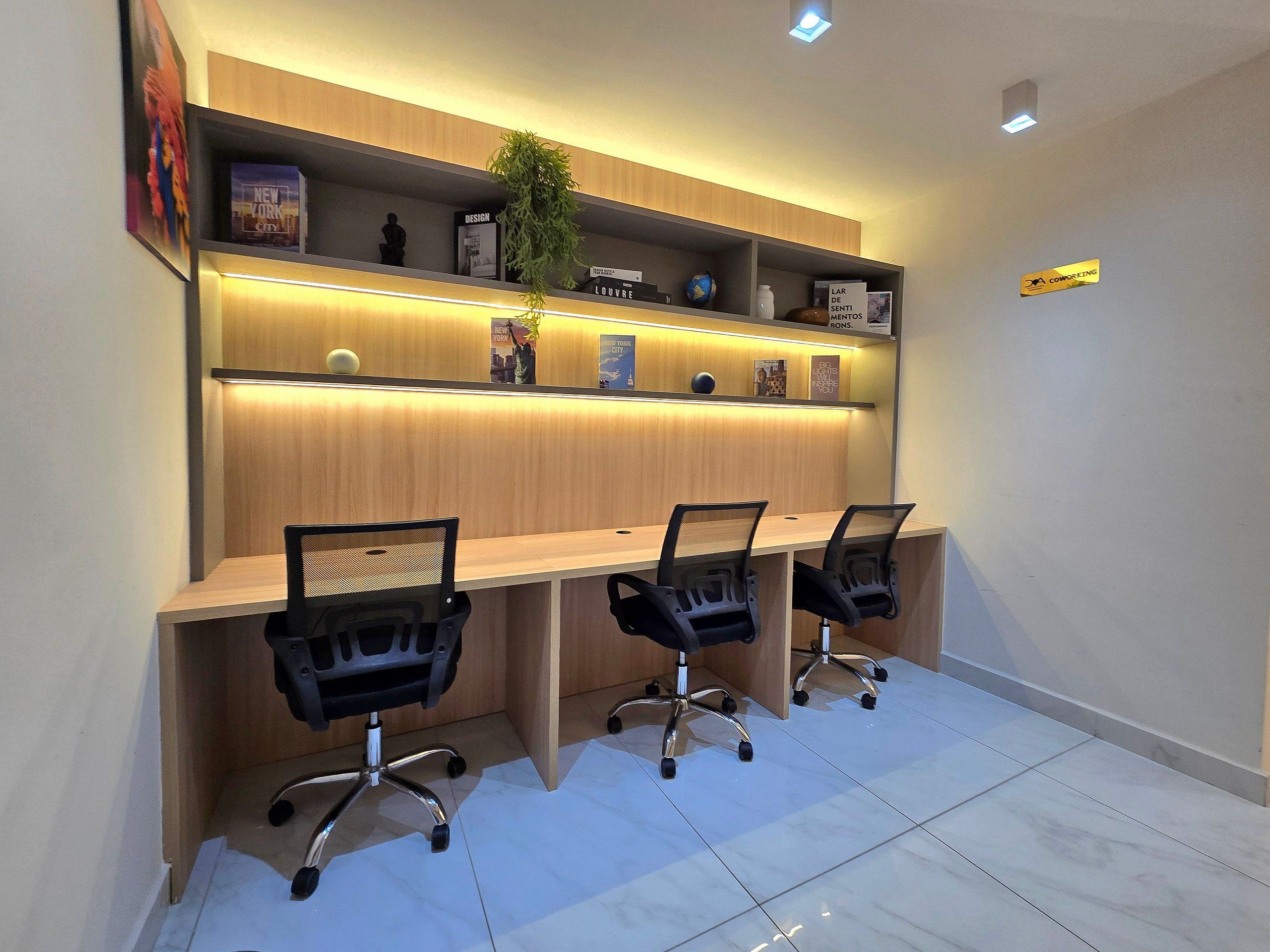 Un salón de conferencias con una larga mesa, tres sillas de oficina y estanterías con libros y objetos decorativos.