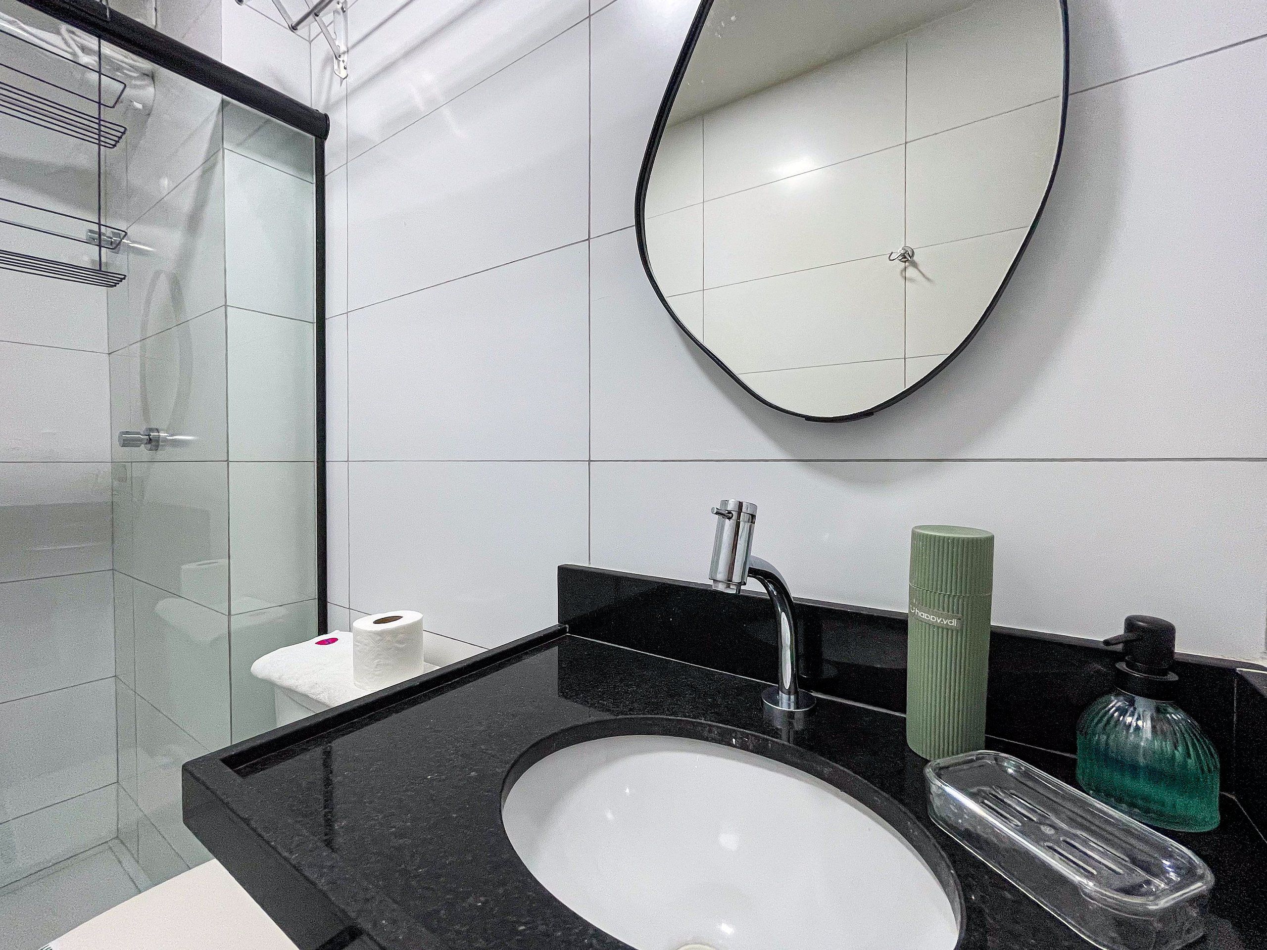 Un baño moderno con cabina de ducha de vidrio, encimera negra, lavabo blanco y espejo.