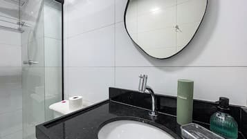 Un baño moderno con cabina de ducha de vidrio, encimera negra, lavabo blanco y espejo.