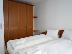 A bedroom with a bed, white bedding, a wooden wardrobe, and a nightstand with a lamp. - Fee-Rien Appartement/Fewo 4-Bettwohnung by Interhome (Saas-Fee)