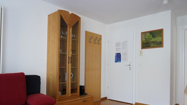 A room with a red sofa, a wooden wardrobe with glass doors, a white door with a picture, and a wooden floor. - Fee-Rien Appartement/Fewo 4-Bettwohnung by Interhome (Saas-Fee)