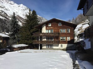 Ein mehrstöckiges Holzhaus mit Balkon, umgeben von schneebedeckten Bergen.