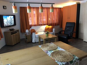 A furnished living room with a sofa, a television, a wooden table, and a chair. - Cresta di Saas Studio, Dusche, WC, Erdgeschoß/Parterre by Interhome (Saas-Grund)