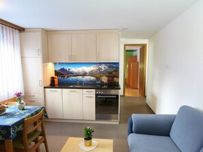 En kompakt opholdsstue med et tekøkken, et spisebord og en sofa.