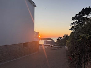 En byggnad med ett sluttande tak, en grusuppfart och utsikt över solnedgången över vattnet.