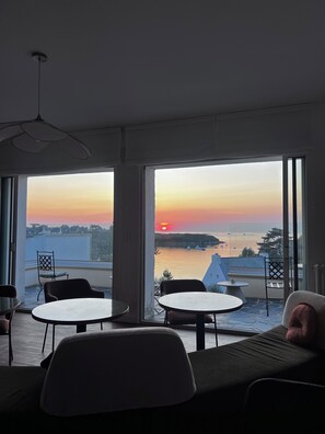 Una stanza con vista sul tramonto su un'area d'acqua, arredata con un divano, due poltrone e un tavolino.