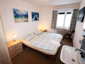 Ein Schlafzimmer mit zwei Betten, einem Nachttisch mit Lampe, einem Fenster mit Vorhängen und einem Badezimmer mit Waschbecken.