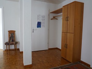 Ein Zimmer mit einem Holzschrank, einem Stuhl und einer Tür mit Aushängen.
