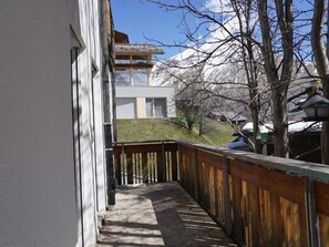 Ein Balkon mit Holzgeländer, Blick auf ein Gebäude mit Schrägdach und einen schneebedeckten Berg im Hintergrund.