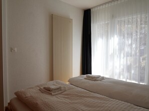 A hotel room with two beds, a radiator, and sheer curtains. - Fee-Rien Appartement/Fewo, Bad, WC 6-Bettwohnung by Interhome (Saas-Fee)