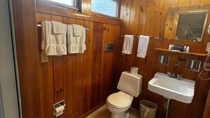 Un baño con paneles de madera, un inodoro, un lavamanos y dos barras para toallas.