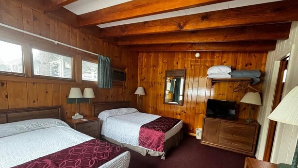 Una habitación tipo cabaña de madera con dos camas, un aparador, un espejo y una televisión.