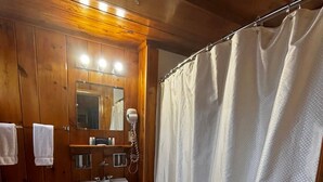 Un baño con paredes de madera, un lavamanos blanco, un inodoro, una cortina de ducha y un espejo.