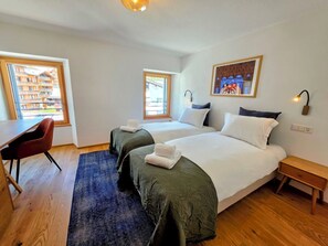 Ein Hotelzimmer mit zwei Betten, einem Schreibtisch, einem Stuhl und Blick auf ein Gebäude durch ein Fenster.