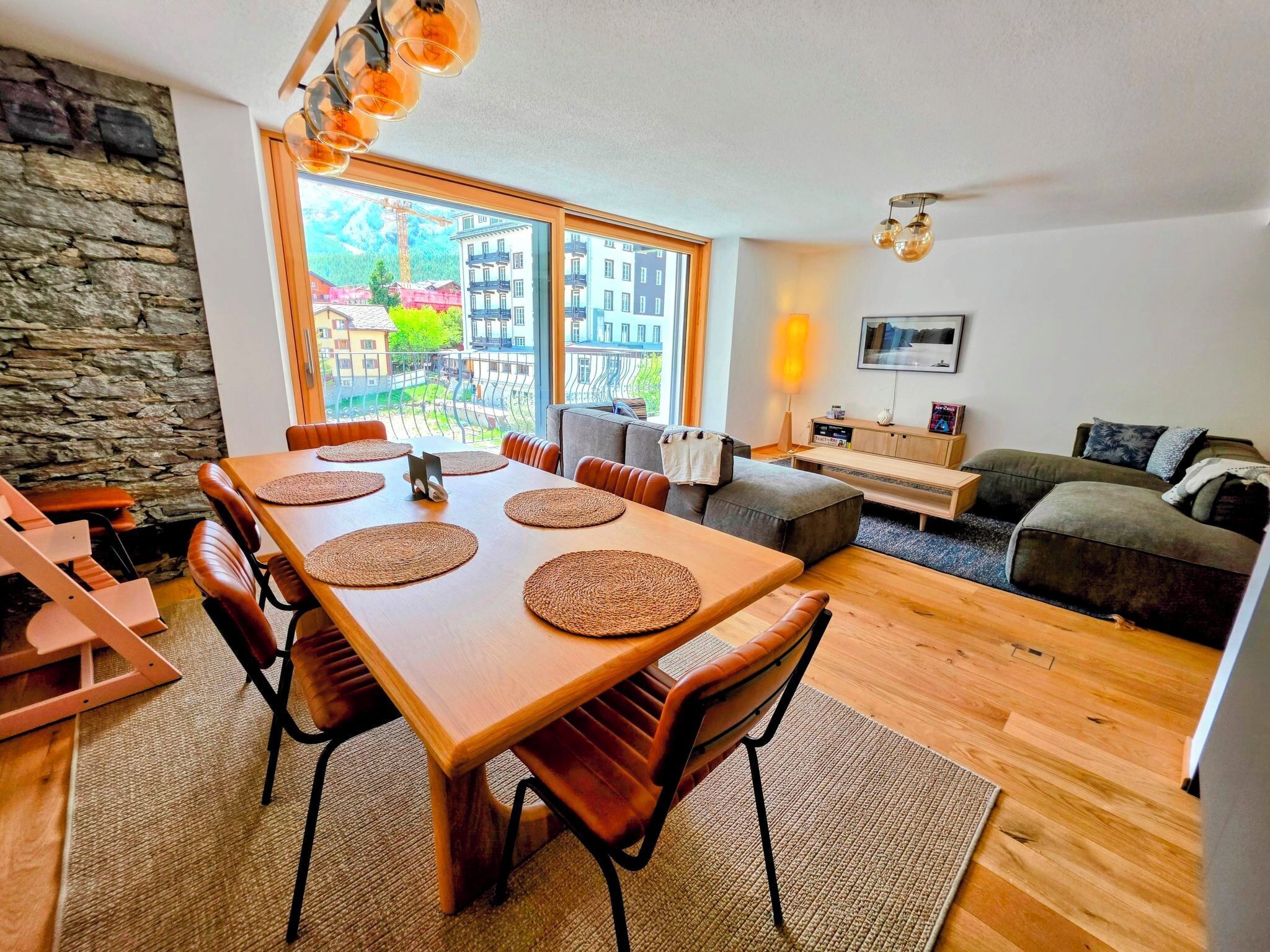 Ein moderner Wohnraum mit Essbereich, Sofa und Blick auf Gebäude durch große Fenster.