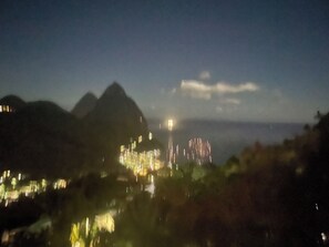 Nachtsicht auf eine gebirgige Landschaft mit beleuchteten Gebäuden und einer fernen Lichtquelle.