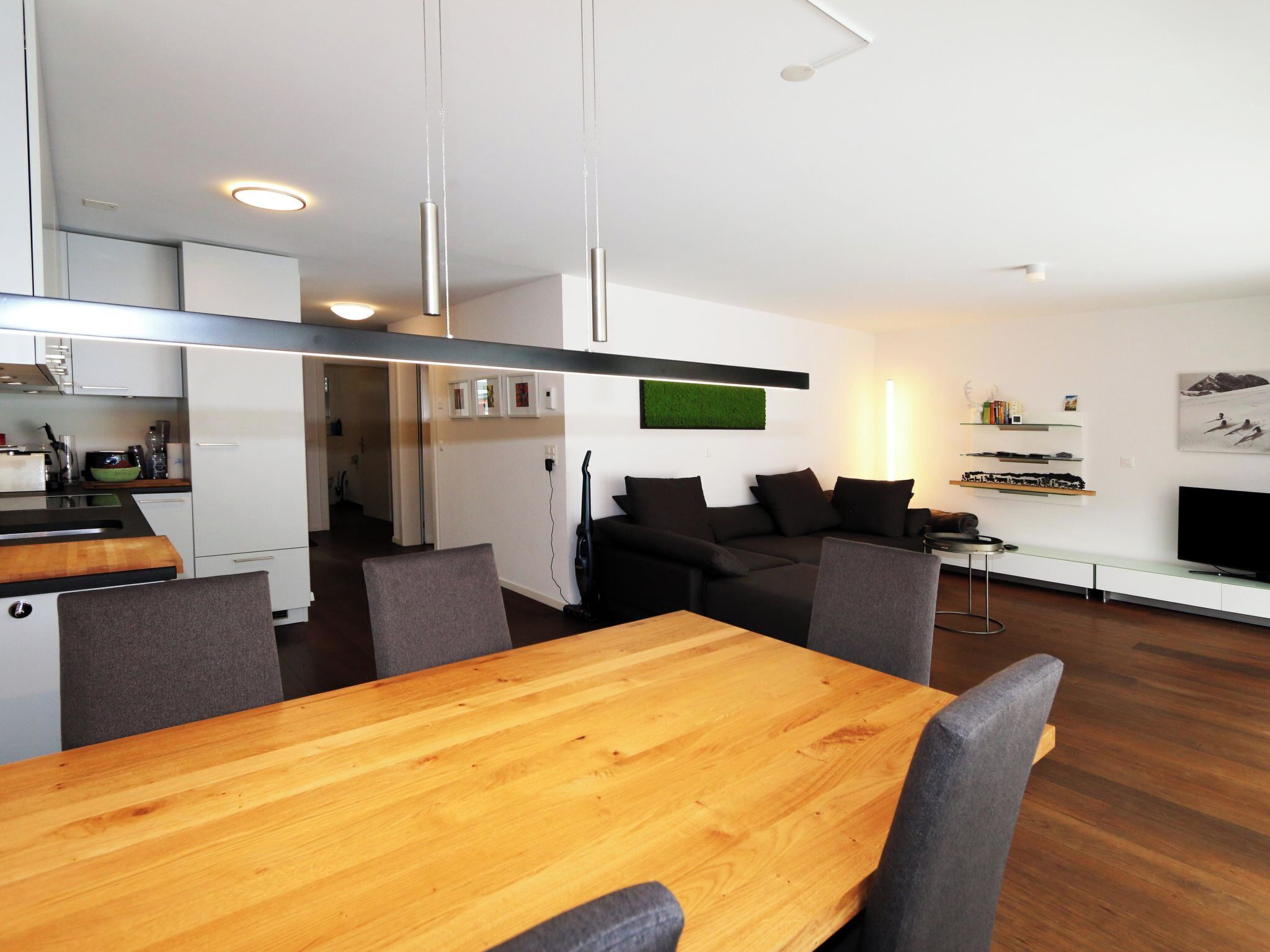 Una cocina moderna con armarios blancos, una mesa de comedor de madera y un sofá negro en la sala.