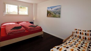 Un dormitori amb un llit, una cadira, una finestra i un quadre a la paret.