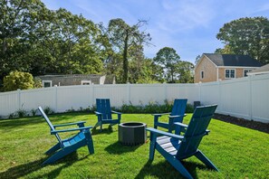 Un jardin avec une clôture blanche, un foyer et des fauteuils Adirondack bleus.