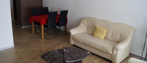 A living room with a sofa, a coffee table, and a dining area with chairs and a table.