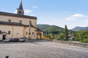Un edificio storico con un campanile, un cortile in pietra e montagne sullo sfondo.