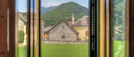 A view through a window of a building with a stone facade, a small balcony, and a mountain in the background.