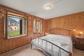 Un dormitorio con cama, paredes de madera, una ventana y vista a un edificio.